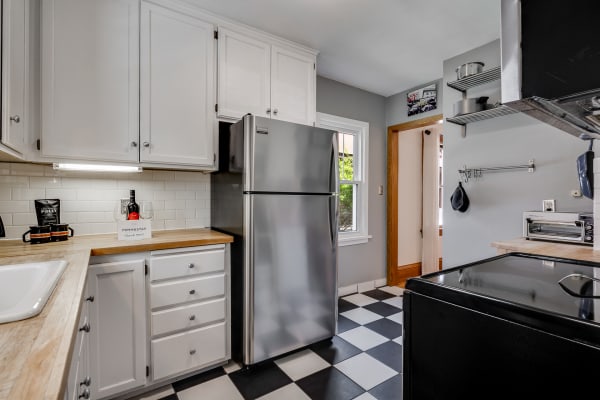 A bright and modern kitchen with white cabinets, a stainless steel fridge, and black and white checkered floor tiles.