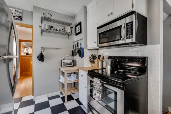 A contemporary kitchen with stainless steel appliances, open shelving, and a checkered floor.