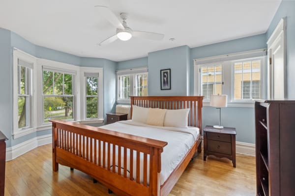 Spacious bedroom with a wooden bed, soft blue walls, and bay windows.