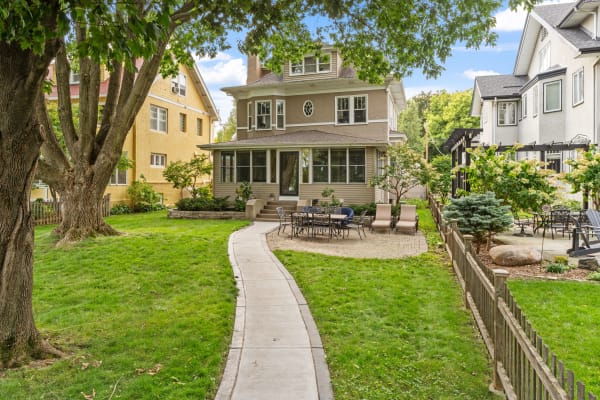 A residential backyard with a stone pathway, outdoor seating, and a multi-story house.