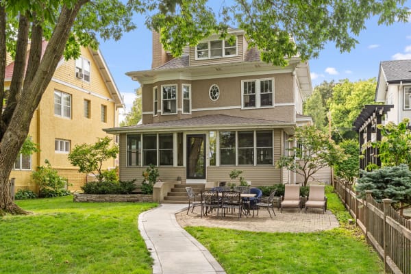A two-story beige house with large windows surrounded by a green lawn and patio.