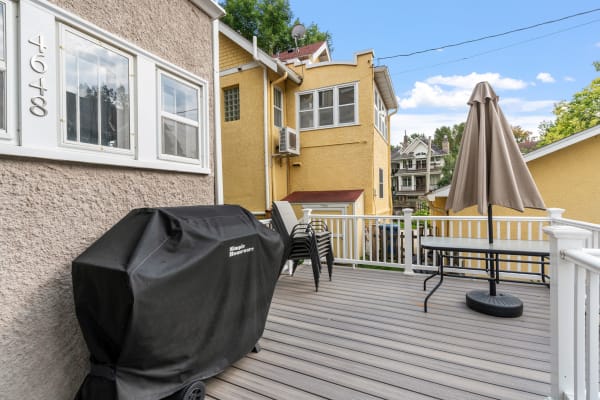 Outdoor deck featuring a grill and table with an umbrella, overlooking nearby buildings.