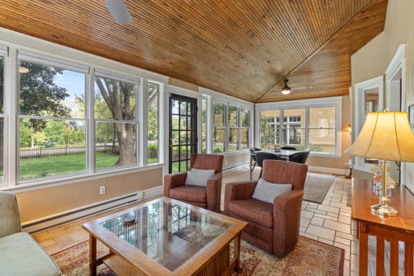 Sunroom with wooden ceiling beams, large windows, and comfortable seating.