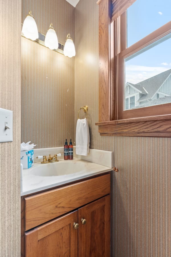 A small bathroom featuring a wooden vanity, light fixtures, and striped wallpaper.