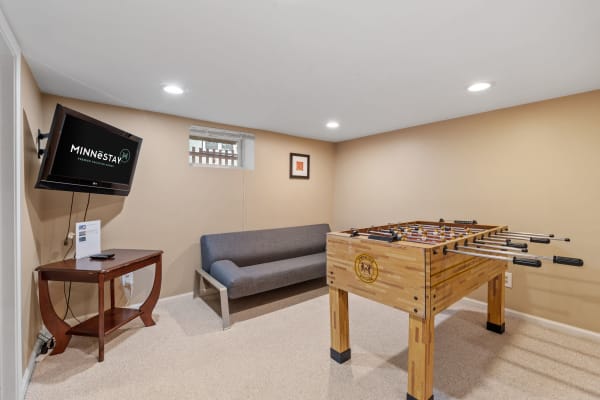 A basement game room with a foosball table, a gray couch, and a mounted TV.