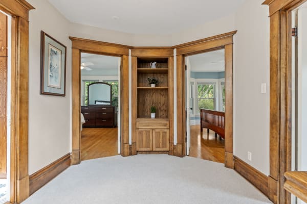 Interior view of a home with wooden trim, carpeted floor, and a built-in shelf in a corner.