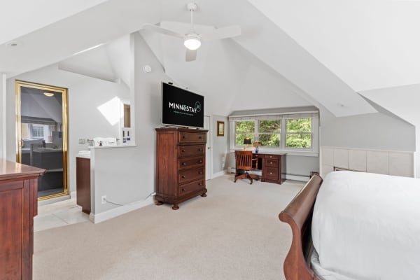 Spacious attic bedroom with a wooden sleigh bed and a workspace, featuring a TV and a shower.