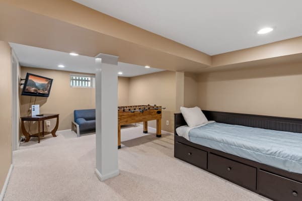 A spacious basement rec room featuring a foosball table, a sofa, and a twin bed.
