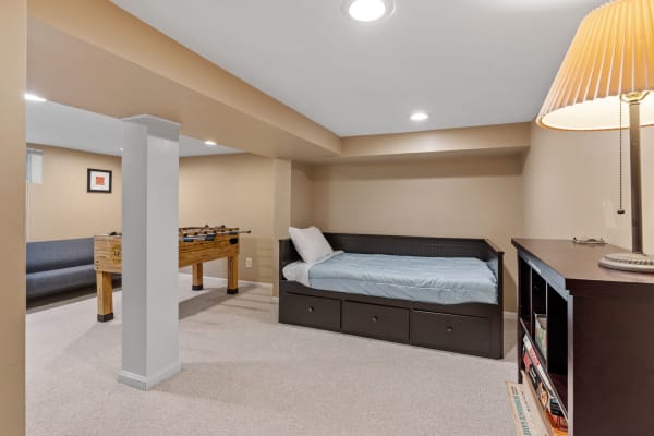 A cozy basement with a daybed, foosball table, and gray sofa against beige walls.