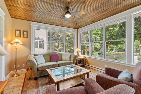 A sunroom with large windows, a green sofa, and a wooden coffee table.
