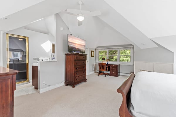 Bright attic bedroom with sloped ceiling, TV, and workspace.