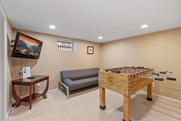 Cozy basement room with a foosball table, a gray sofa, and a television displaying a mountain landscape.