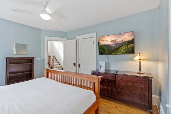 A bedroom featuring a wooden bed, dresser, ceiling fan, and flat-screen TV displaying a landscape.