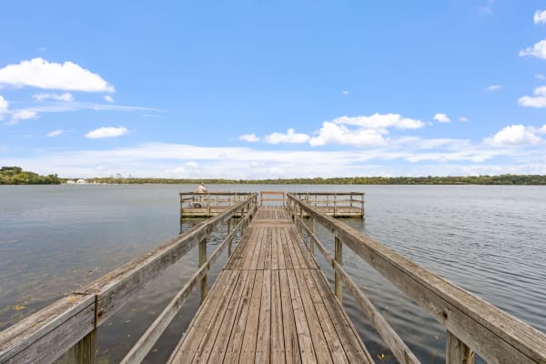 A wooden pier leading into a tranquil lake with a person seated at the end.