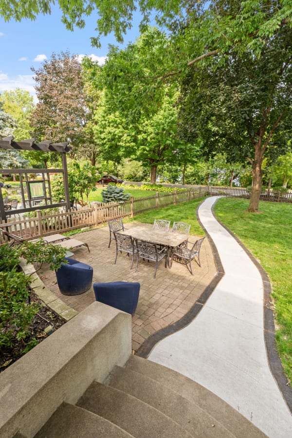 A garden patio with a dining table surrounded by chairs, a winding pathway, and lush trees.