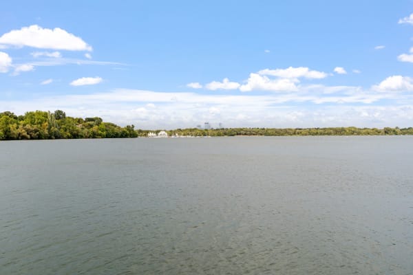 A wide lake surrounded by greenery and a distant city skyline under a blue sky.