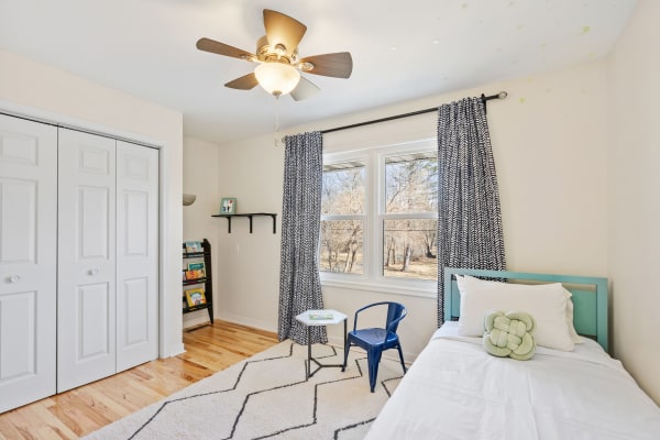 Cozy bedroom featuring a bed, blue chair, side table, and shelves filled with books.