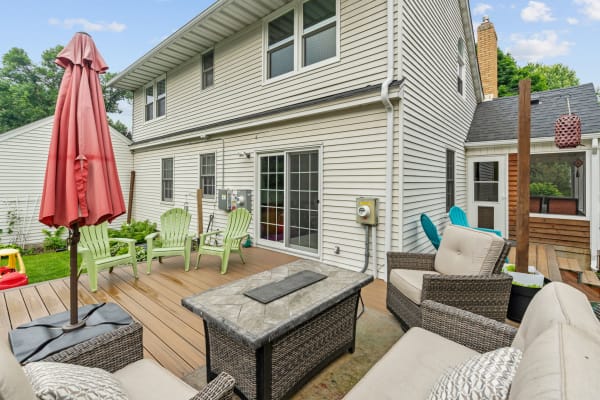 A backyard patio with green chairs and a red umbrella in front of a house.
