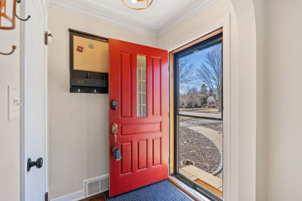 A red door open to an entryway, featuring a wall-mounted organizer and a view of the outdoors.