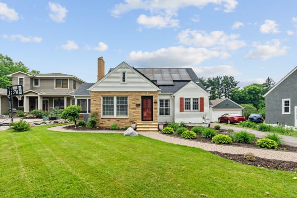 A residential home featuring stone and siding, solar panels, a red door, and landscaped gardens.