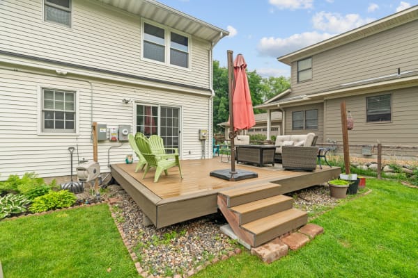 Outdoor deck with green chairs and a pink umbrella, surrounded by grass and plants.