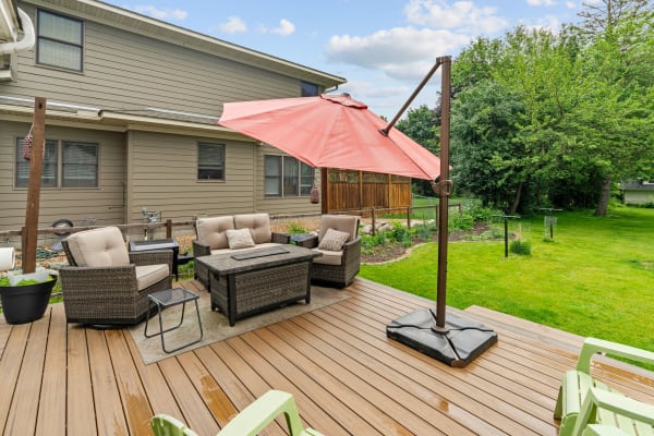 An outdoor patio with lounge chairs, a coffee table, and a large umbrella, surrounded by greenery.