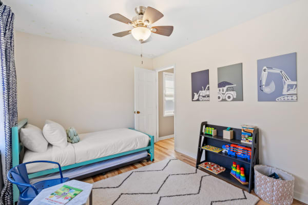 A children's bedroom featuring a turquoise bed, framed construction vehicle art, and a black toy shelf.