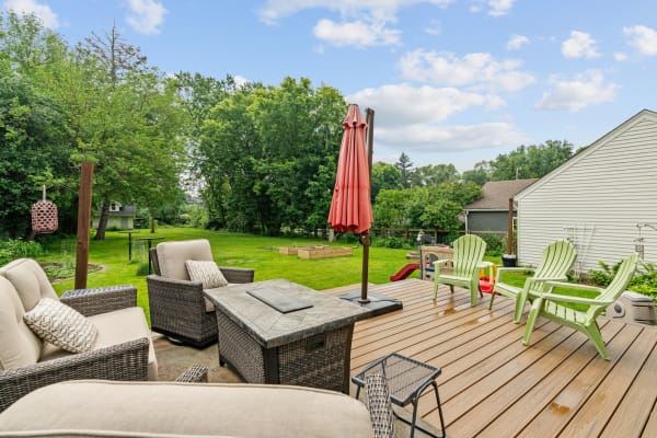 A spacious deck with stylish seating and a patio umbrella set in a vibrant green backyard.
