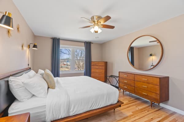 A cozy bedroom featuring a large bed with white linens, wooden furniture, and elegant lighting.