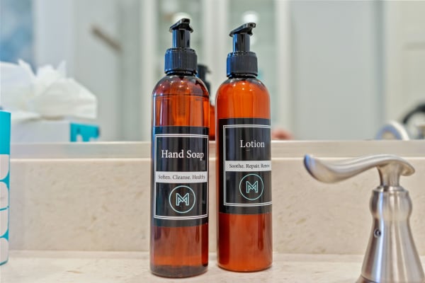 Two amber bottles labeled 'Hand Soap' and 'Lotion' on a light stone countertop.