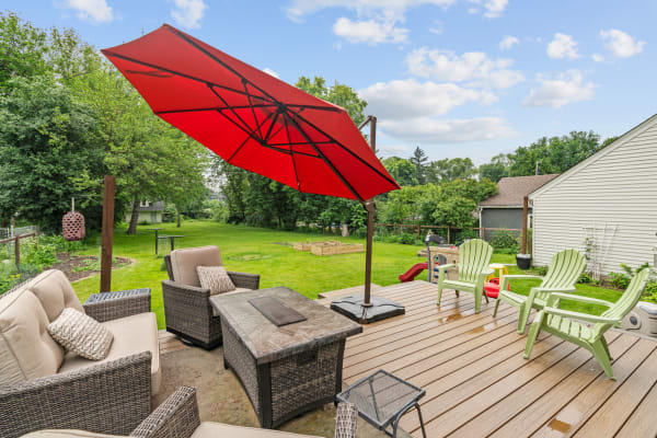 Deck with a red umbrella overlooking a green backyard with seating.