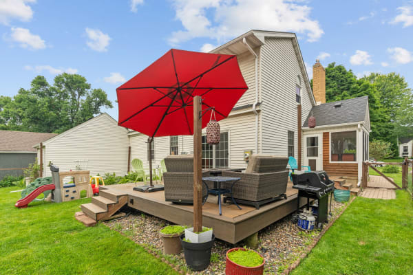 Backyard with a wooden deck, red umbrella, wicker chairs, and a play structure.