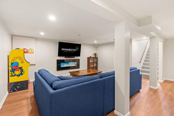 Cozy basement living room with a blue couch, arcade game, and electric fireplace.