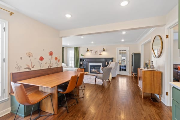 Open-concept dining area with wooden table and chairs, floral wall art, and living room with fireplace.