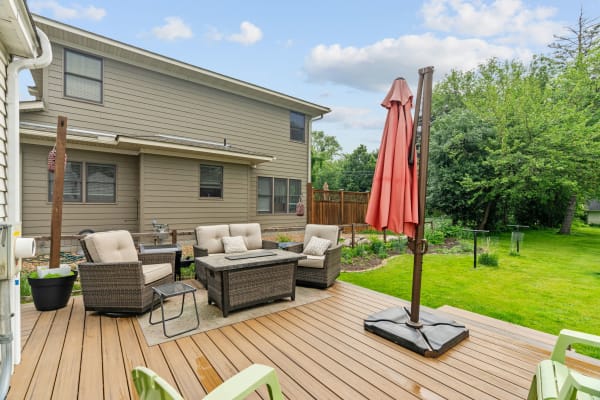 Patio area with beige chairs and a red umbrella next to a well-kept lawn.