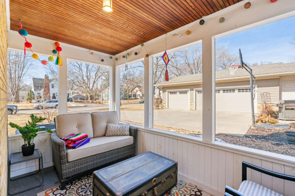 A sunny porch featuring a beige sofa, colorful decorations, and a view of a suburban neighborhood.