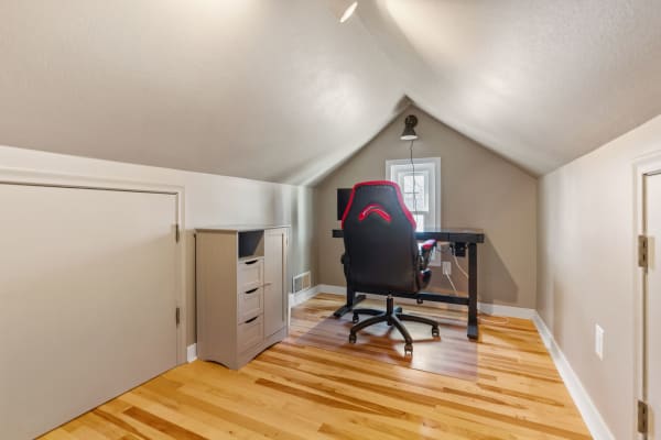 A compact attic workspace with a desk, gaming chair, and light gray storage cabinet.
