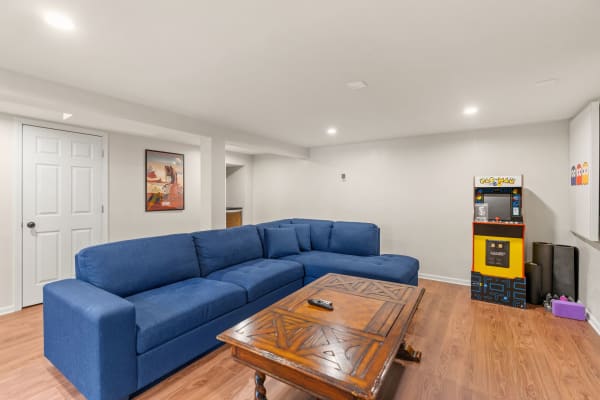 Cozy basement with blue sectional couch, wooden coffee table, and Pac-Man arcade machine.