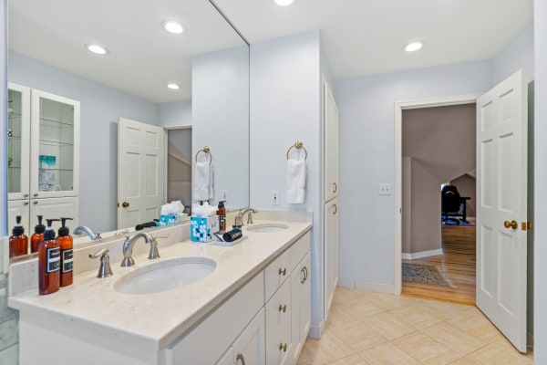 Bright bathroom featuring a double sink vanity, toiletries, and a glass cabinet.