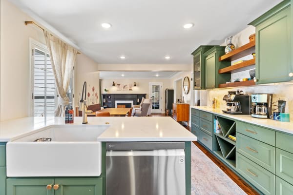 Modern kitchen with green cabinets, white farmhouse sink, and an open layout leading to a living space.