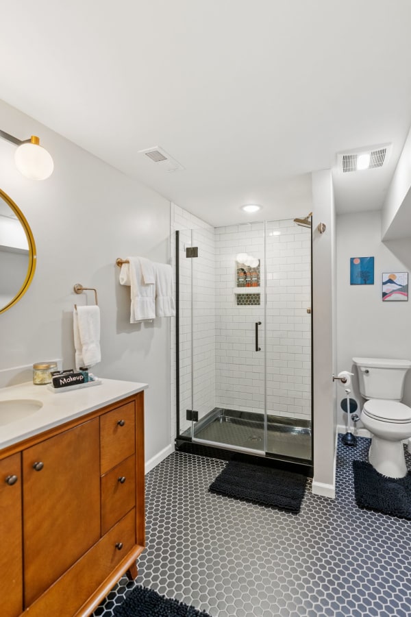 Modern bathroom with glass shower, wooden vanity, and hexagonal flooring.