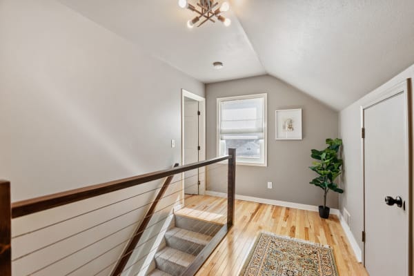 Interior view of a modern hallway with a staircase, light fixture, and potted plant.
