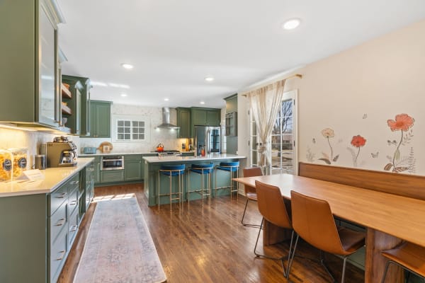 A modern kitchen featuring green cabinets, a breakfast nook, and floral wall art.