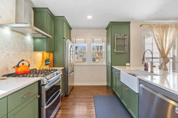 Modern kitchen with green cabinets, stainless steel appliances, and an orange kettle on the stove.