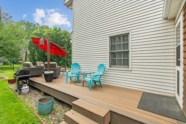 An outdoor deck featuring turquoise chairs, a grill, and a red umbrella among greenery.