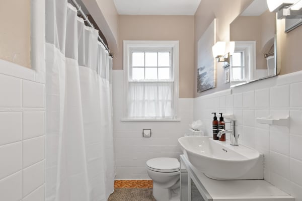 Modern bathroom with white tiles, a contemporary sink, and a window with sheer curtains.
