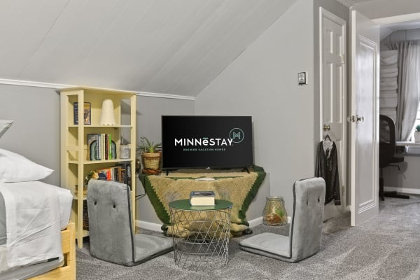 A bedroom corner featuring a bed, television, bookshelf, and floor chairs.