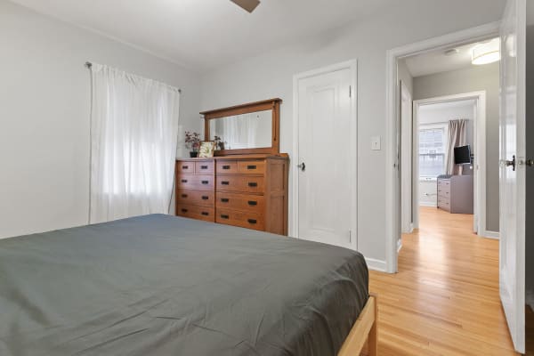 Cozy bedroom with gray bedspread and wooden dresser against light gray walls.