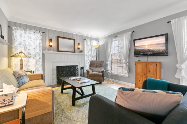 A bright living room with a fireplace, comfortable seating, and a TV displaying a beach scene.
