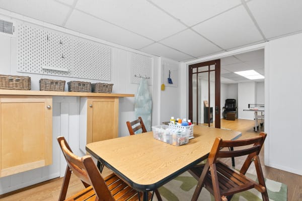 A basement craft area with a wooden table, folding chairs, and organized storage.